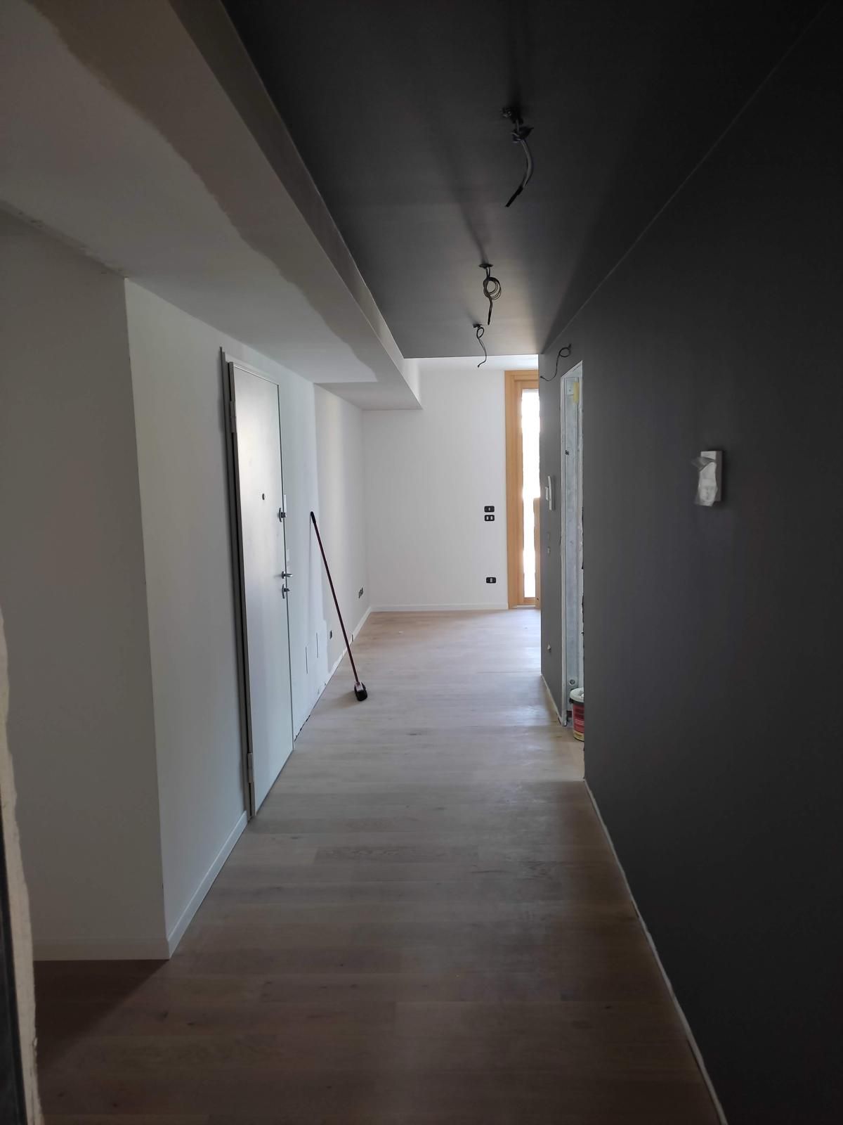 Ingresso con parete grafite, pavimento chiaro e punti luce a soffitto.